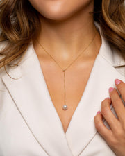 A delicate gold chain with a single, lustrous round pearl sits on woman’s decolette