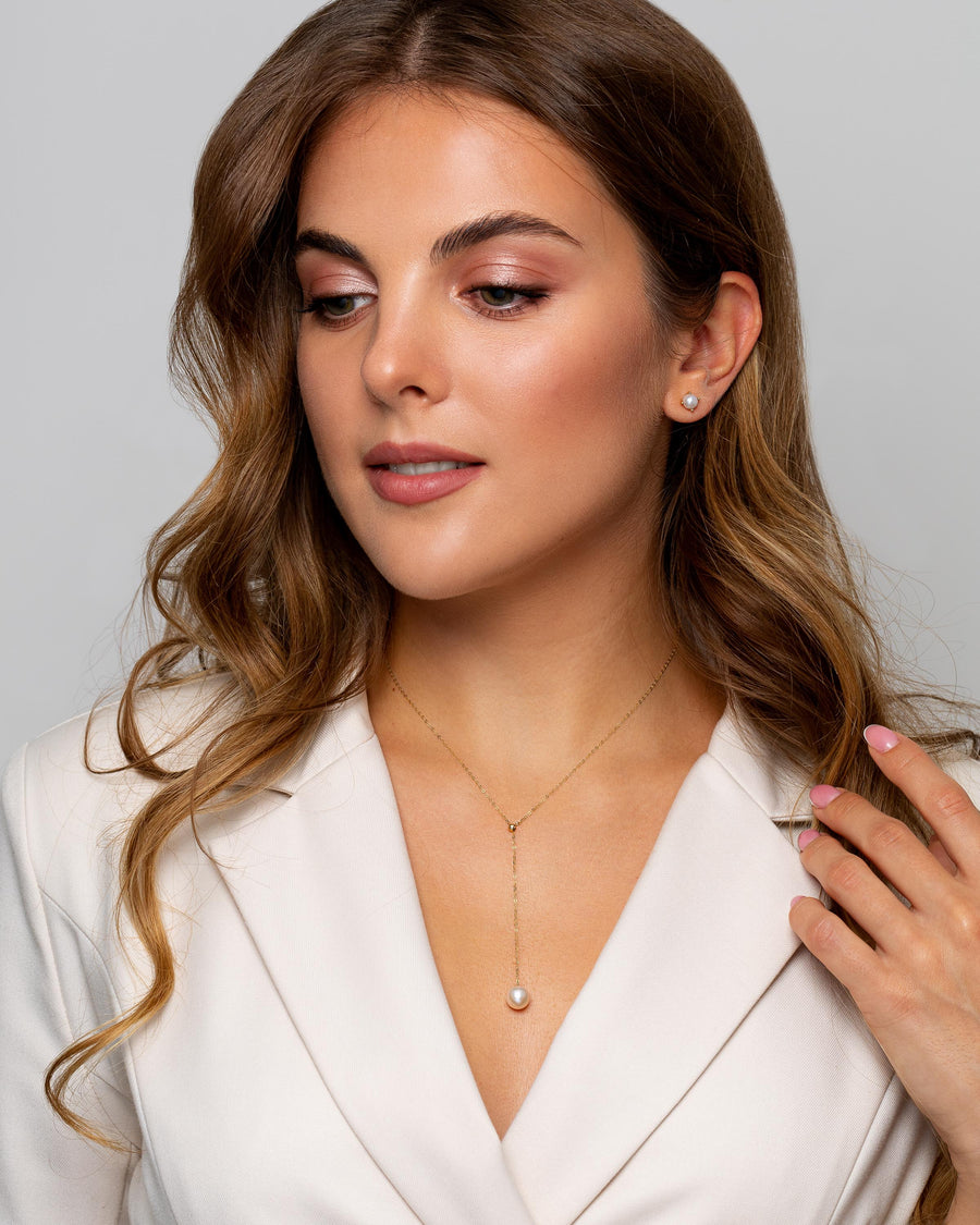 A woman wears delicate Mila prong set gold earrings with pearl.