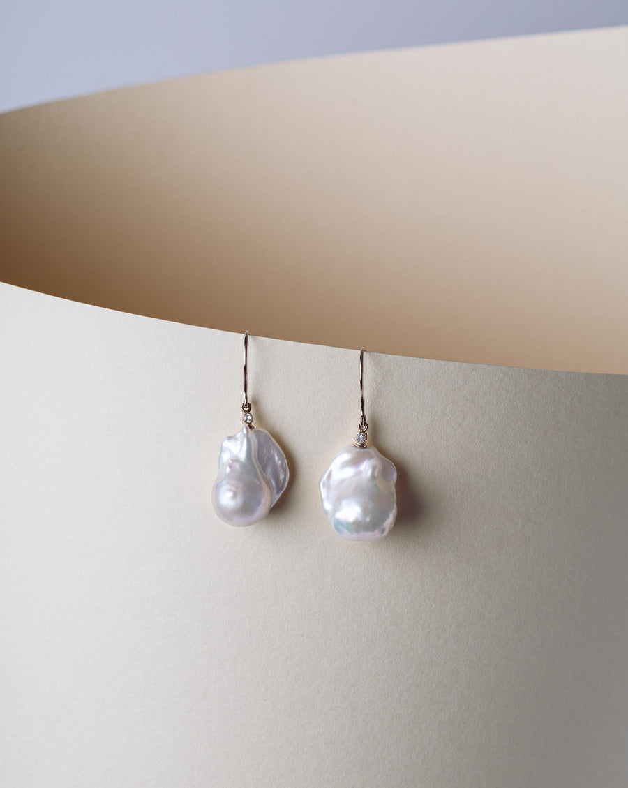 0.06ct bezel set white topaz sits atop large Baroque pearls in the set of drop gold earrings