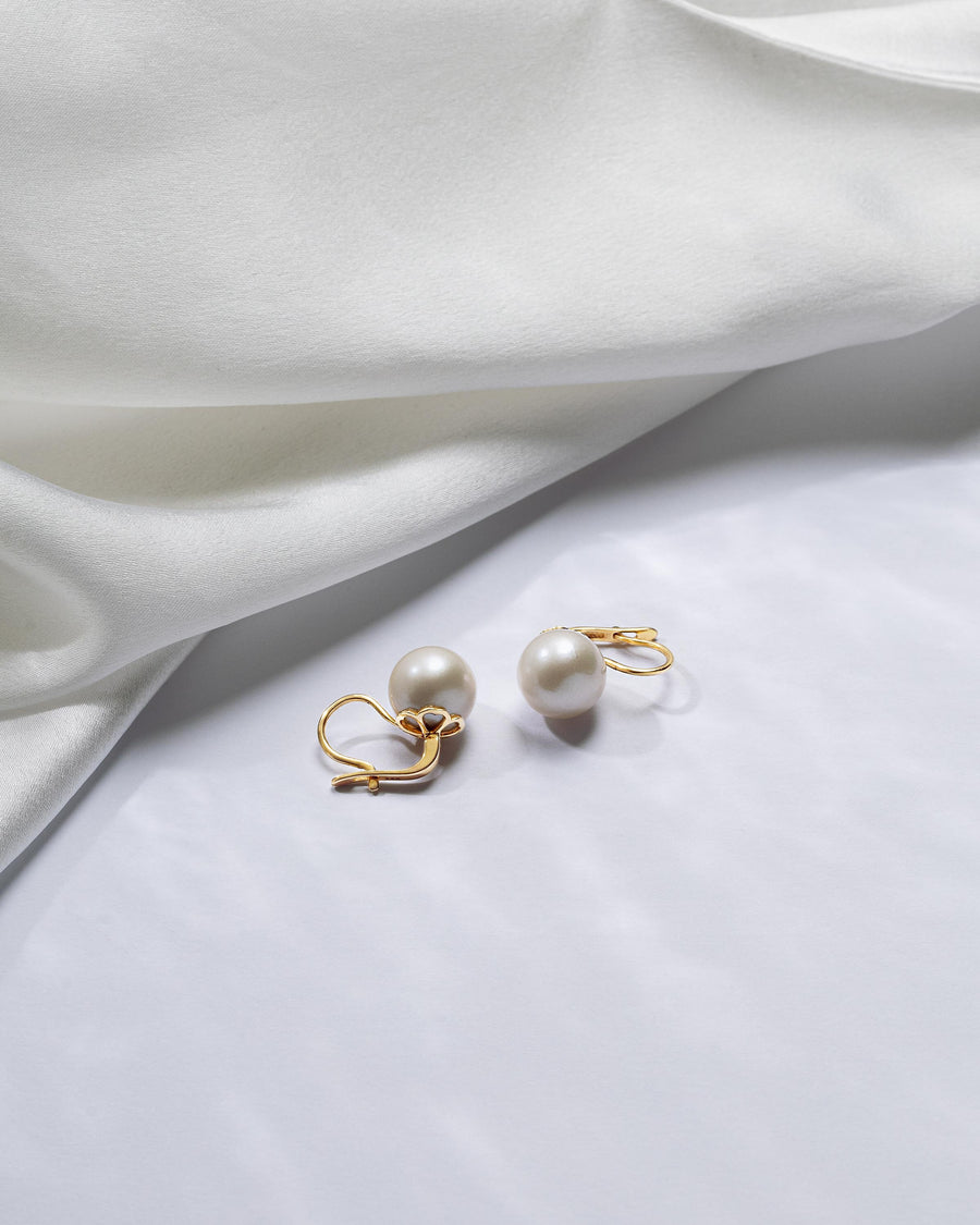The gold leverback earrings with a single, large Edison freshwater pearl lie on white background