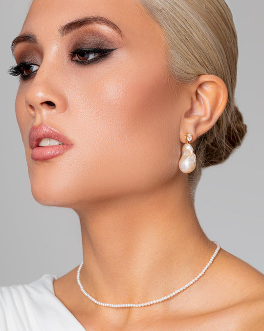 An Asian woman wears the gold stud statement earrings with their glittering AAA grade topaz and lustrous pearl-drop