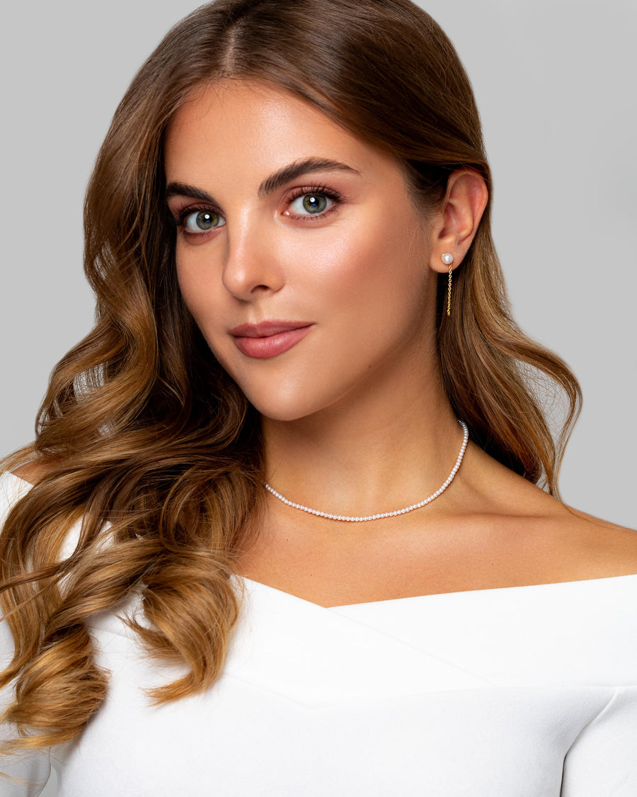 A woman wears transformable 14k gold stud chain earrings with AAA grade round pearl